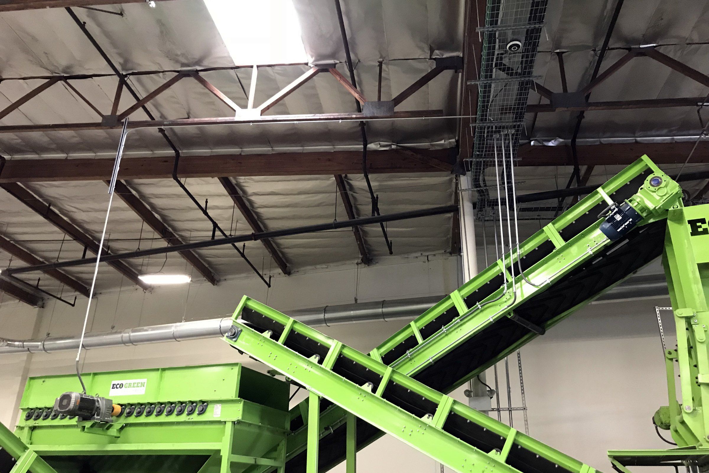 Green tire-recycling conveyors under a warehouse roof, with cable trays overhead