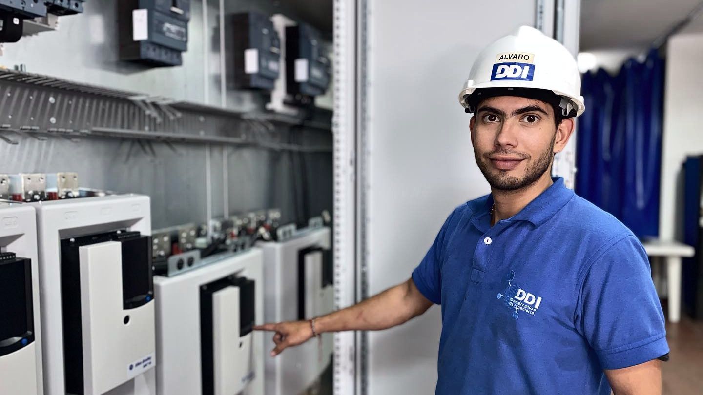 DDI technician in a DDI polo and hard hat beside Allen-Bradley PowerFlex drives in a control panel